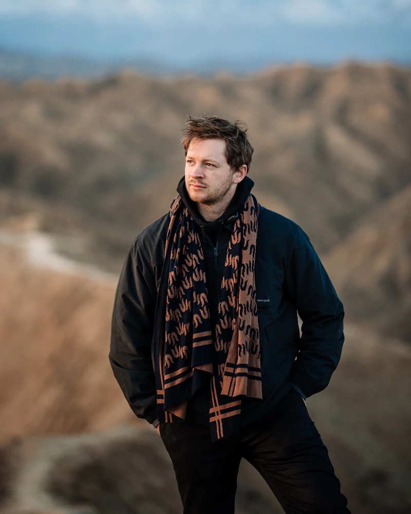 A man in a warm jacket and scarf standing in dry hills