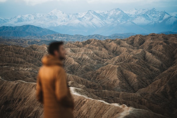 Man in orange coat overlooking arid, mountainous landscape