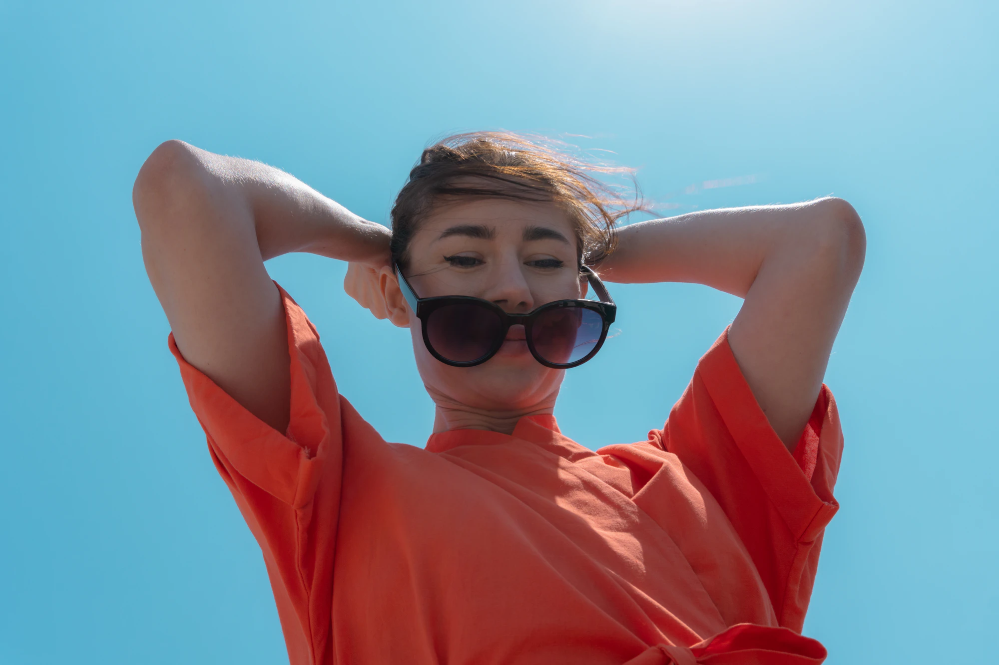 Low-angle portrait in an orange shirt against a blue sky