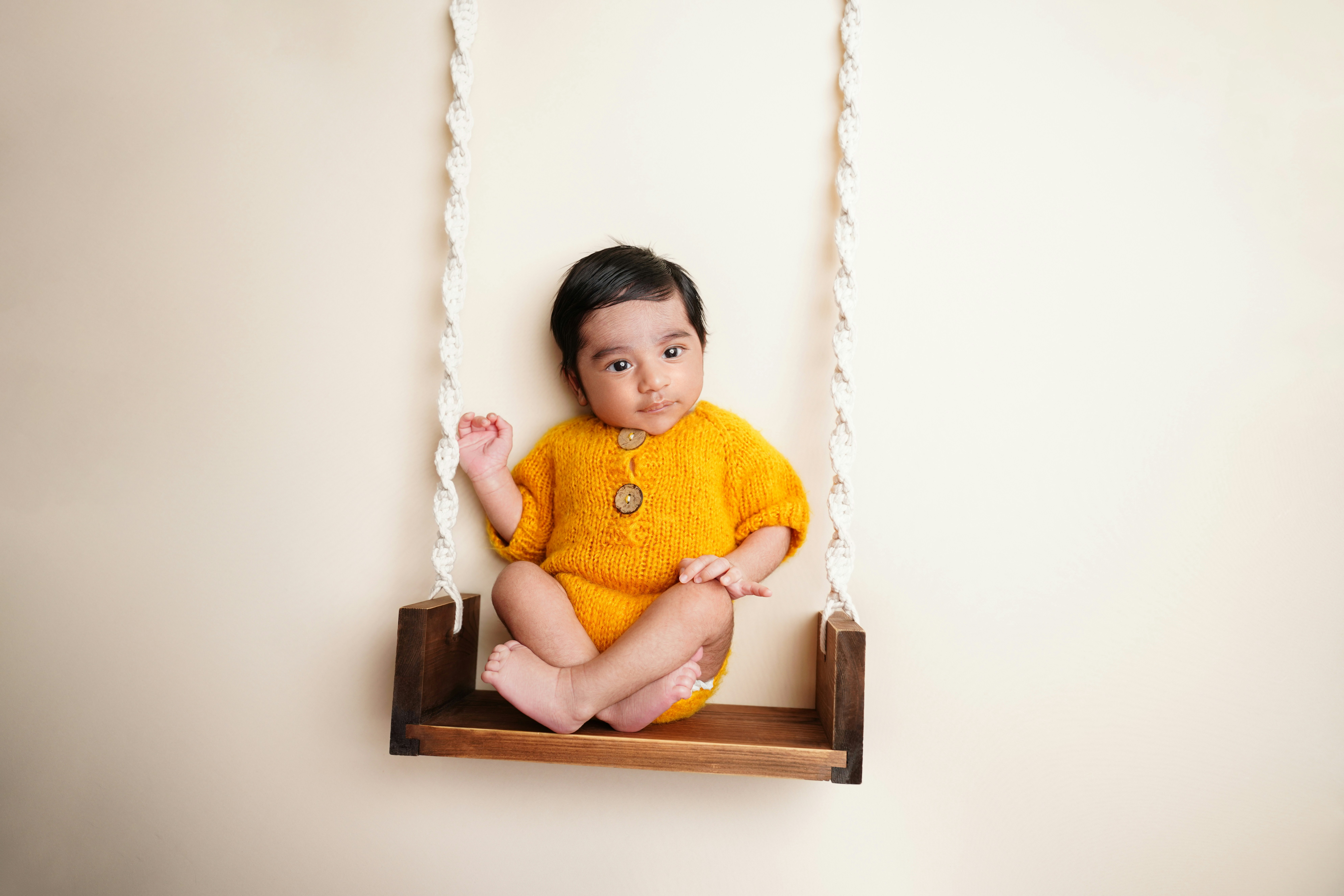A baby in a yellow outfit sits on a swing.