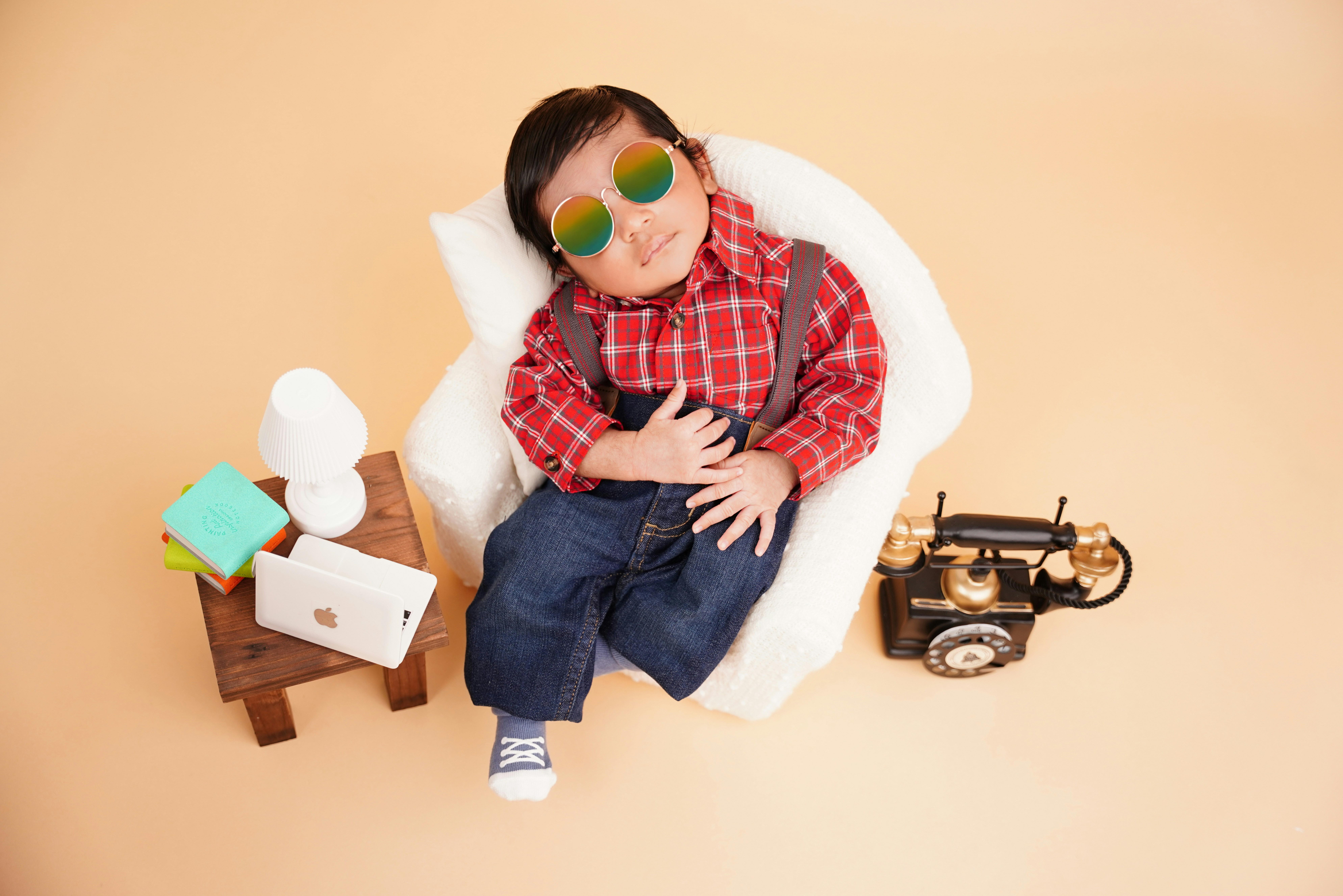 Baby in sunglasses and plaid shirt relaxing on chair.