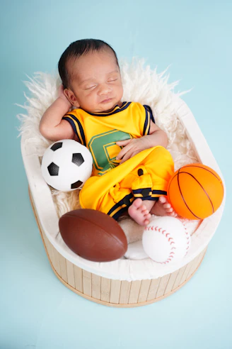 Newborn baby sleeping with sports balls in basket