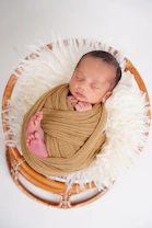 Newborn baby sleeping wrapped in a tan blanket.