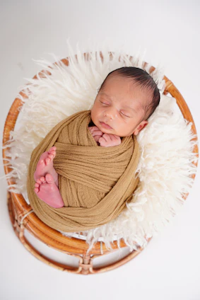 Newborn baby sleeping wrapped in a tan blanket.