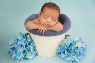 Newborn baby sleeping peacefully in a bucket with flowers.