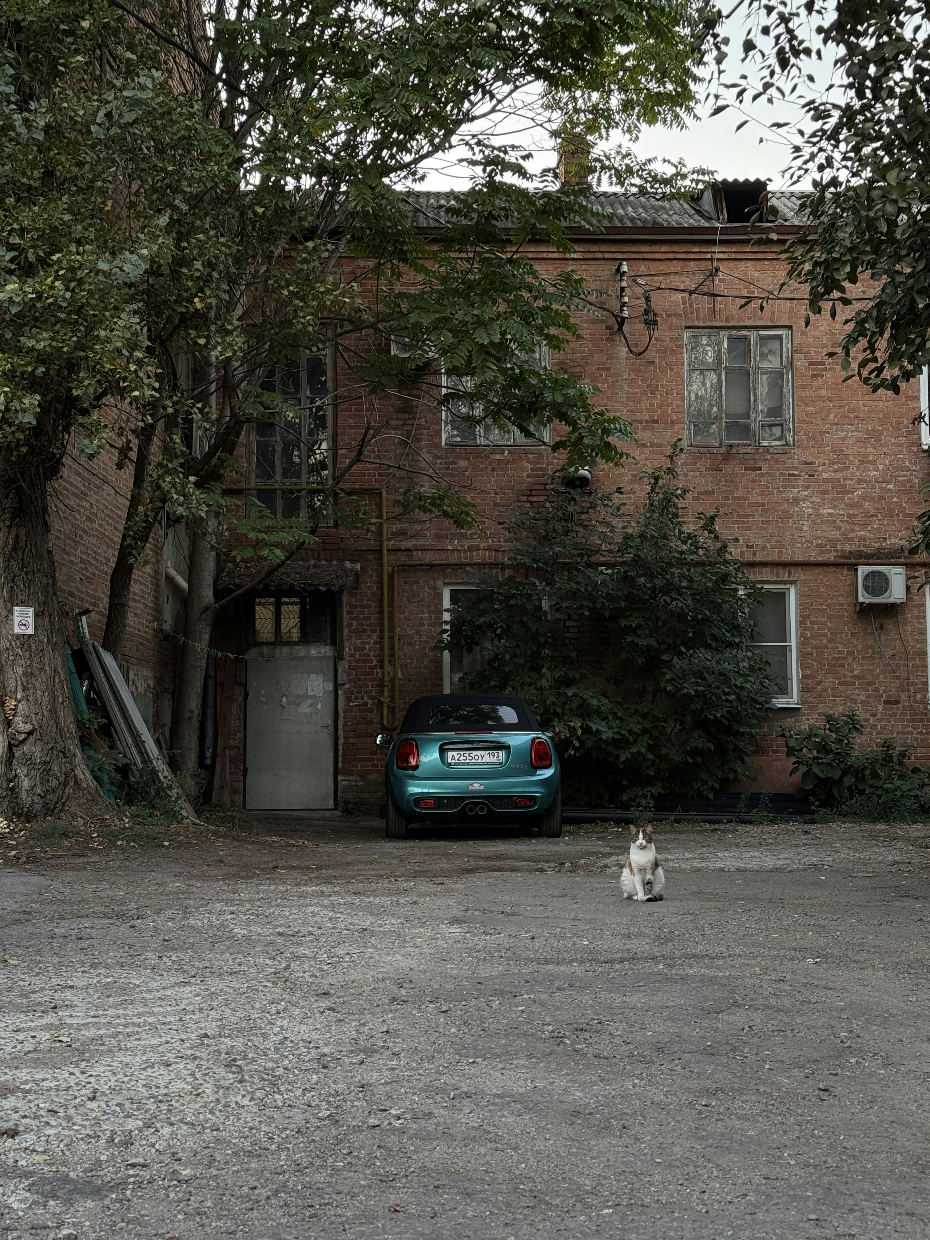 A teal car parked in front of a brick building.