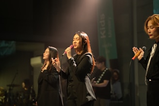 Three singers performing on stage with microphones.