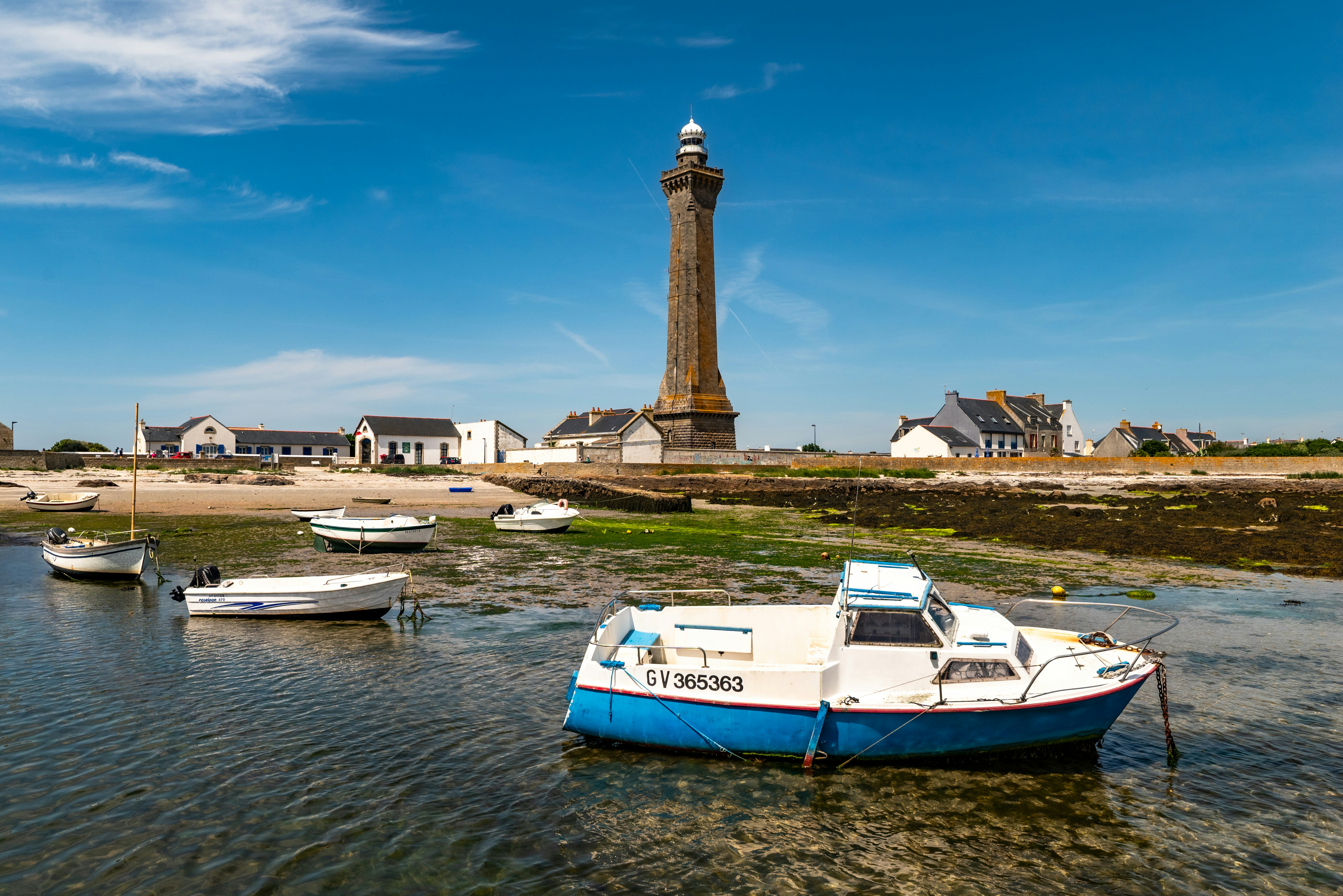 Boats moored near a tall lighthouse and coastal buildings.