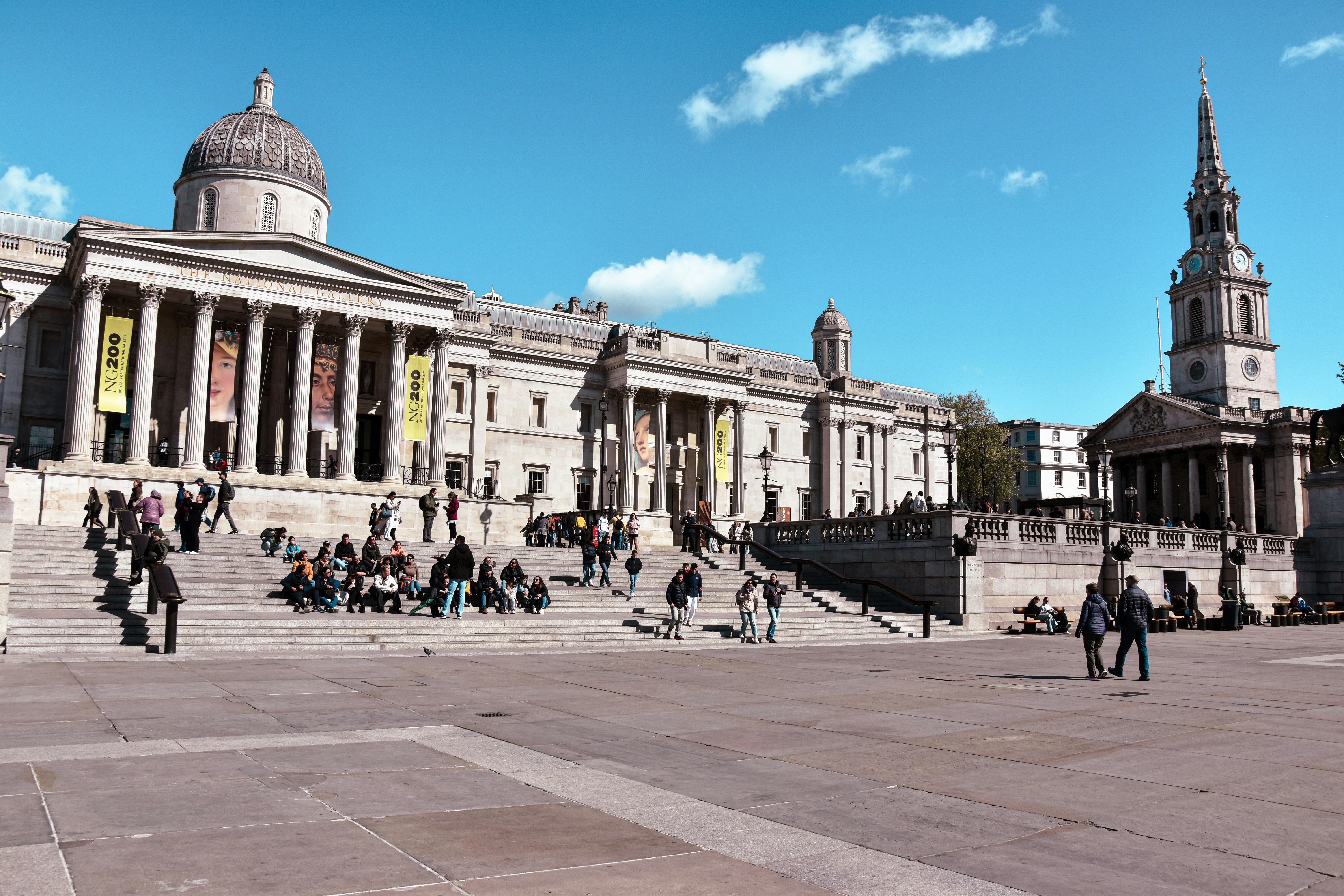 People gathered on steps of grand building under blue sky