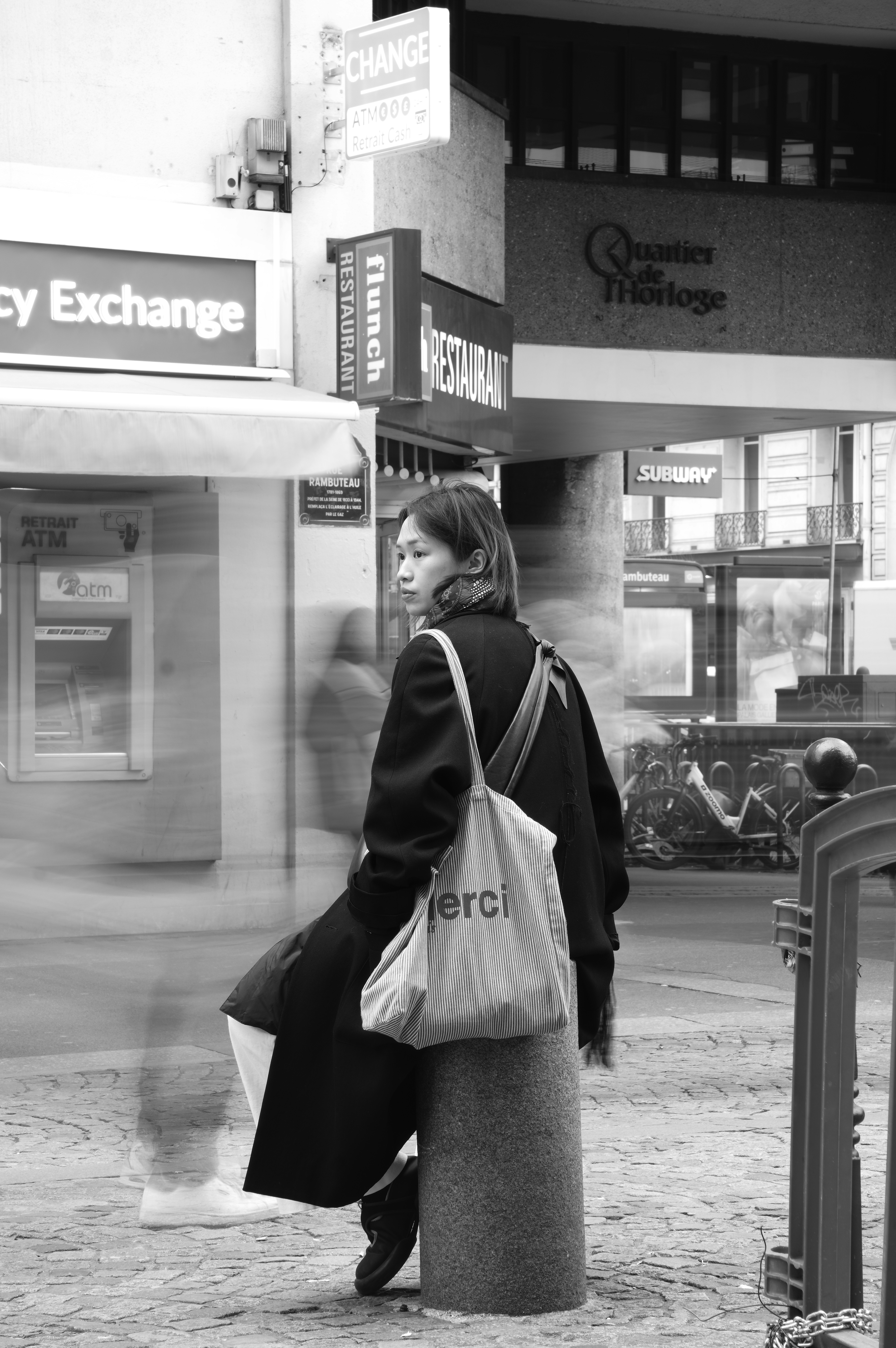 Woman with bag sits on pillar in city street