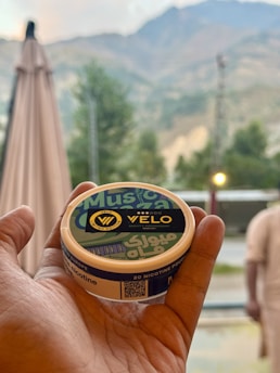 Hand holding a velo nicotine pouch container outdoors