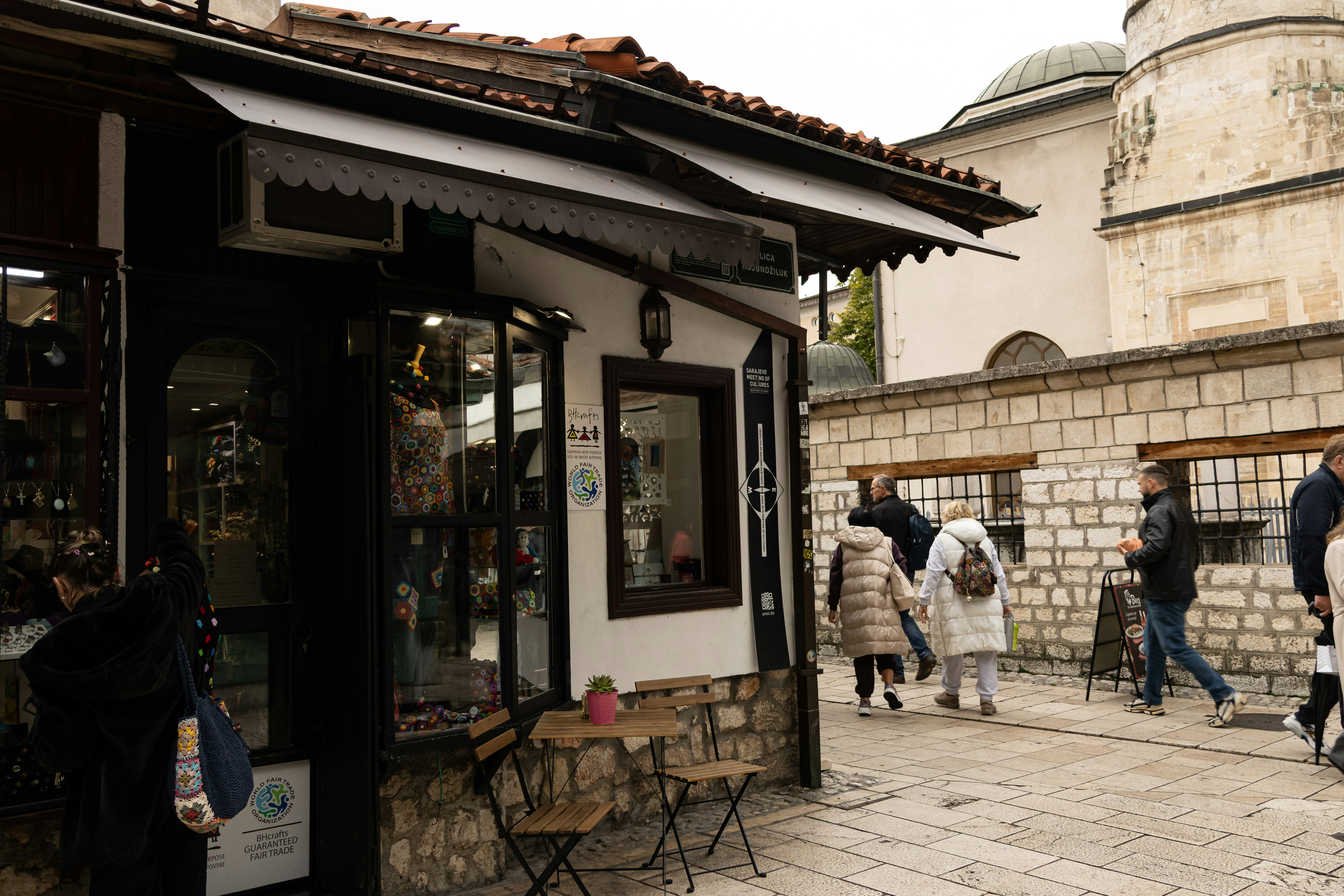People walk past shops on a cobblestone street.