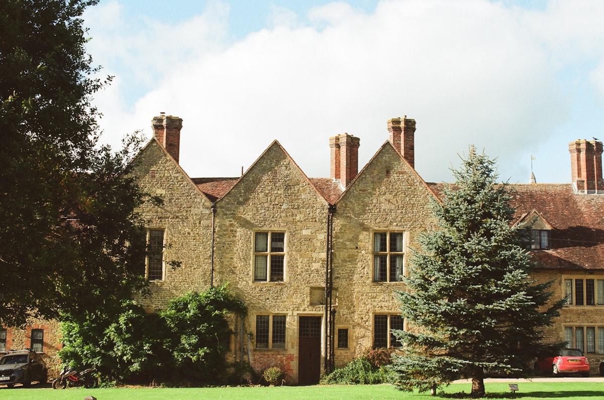 Historic stone manor house with tall chimneys and trees.