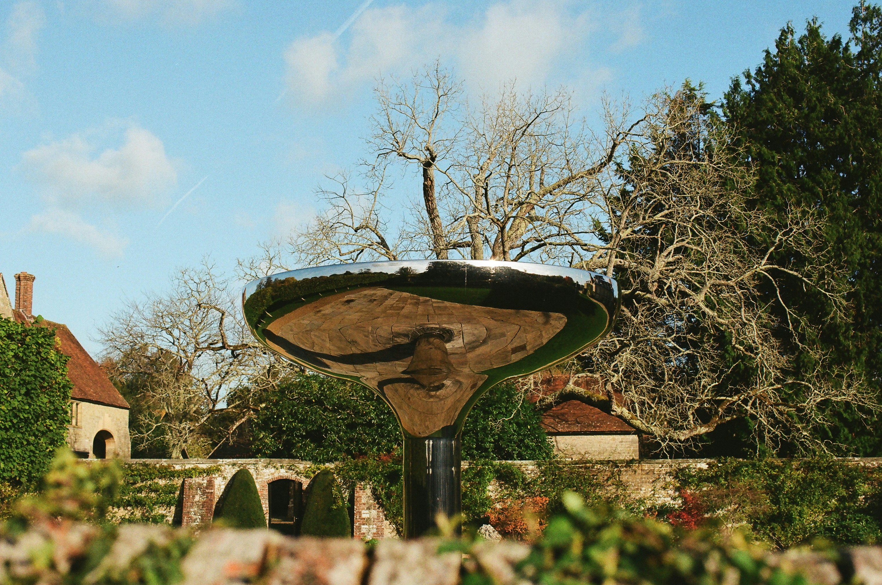 Modern sculpture reflects bare trees and building