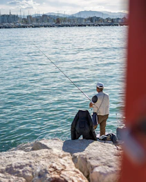 Man fishing from rocky shore with city in background