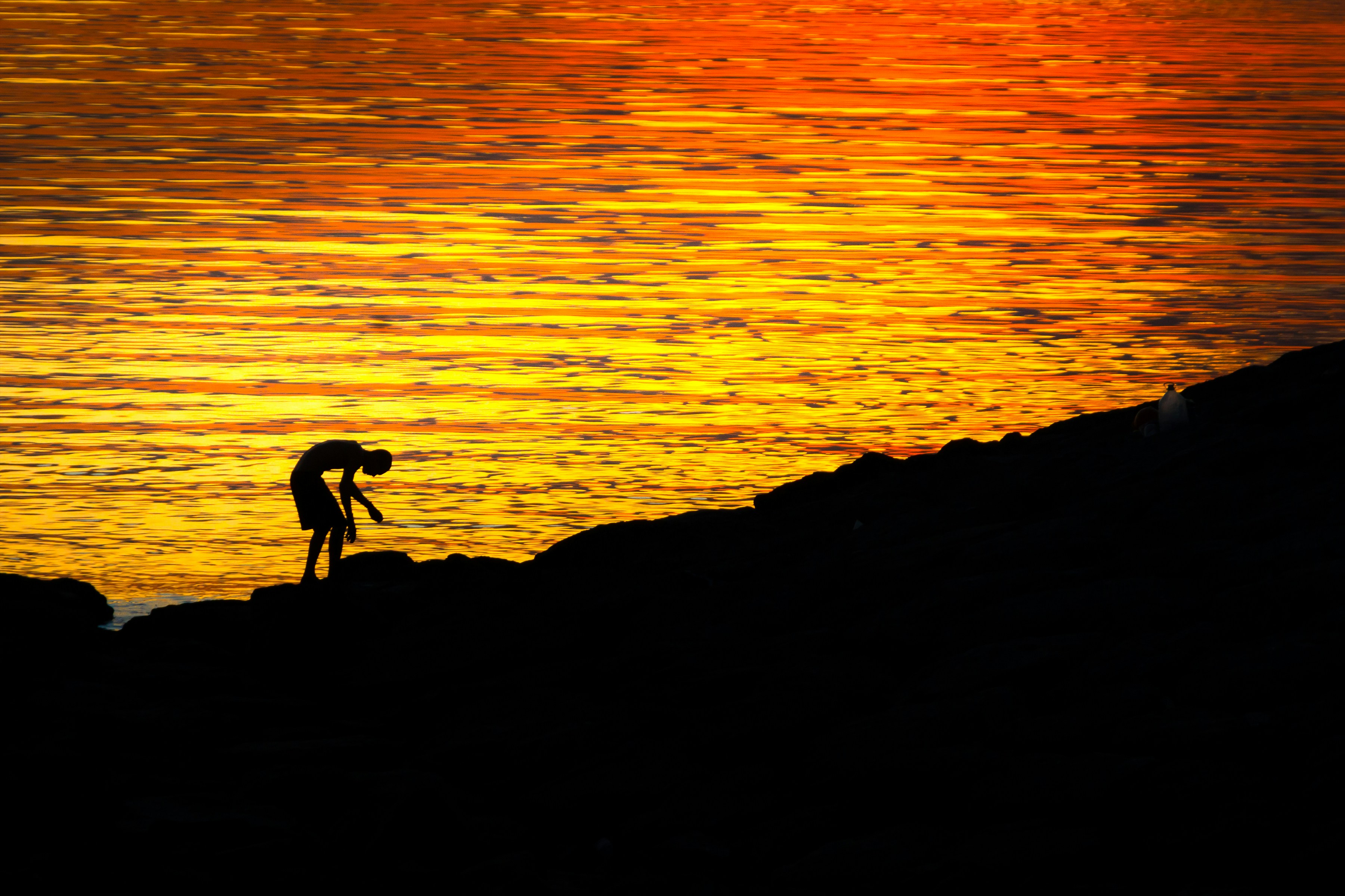 Silueta de una persona en una orilla rocosa al atardecer.