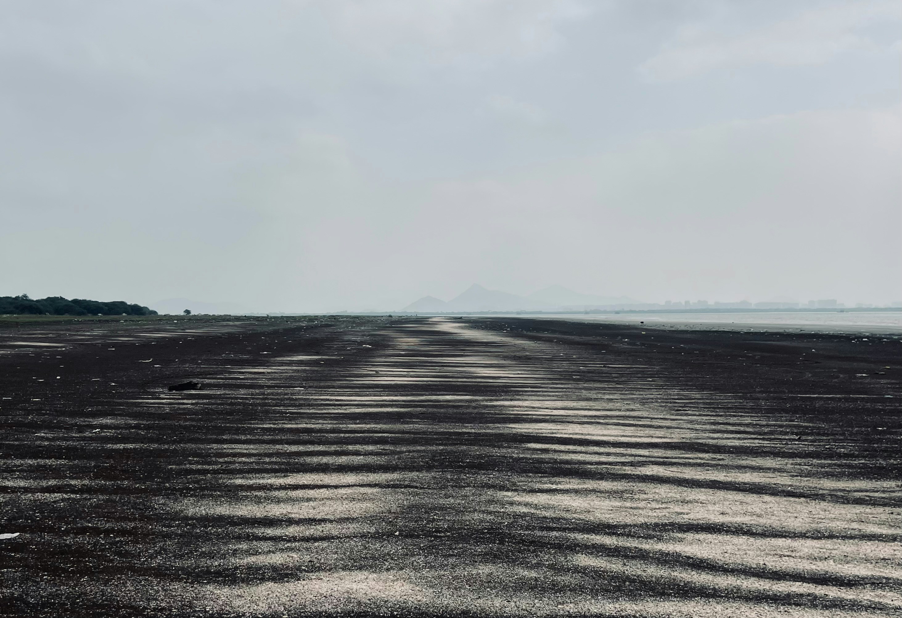 Wet sand path leading to distant mountains under cloudy sky