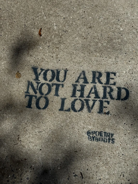 Text on concrete reads "you are not hard to love."