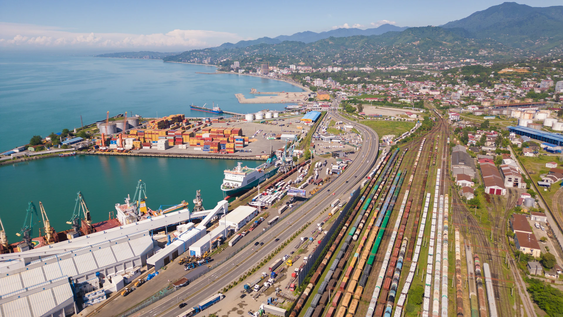 Busy port with ships, containers, and train tracks.