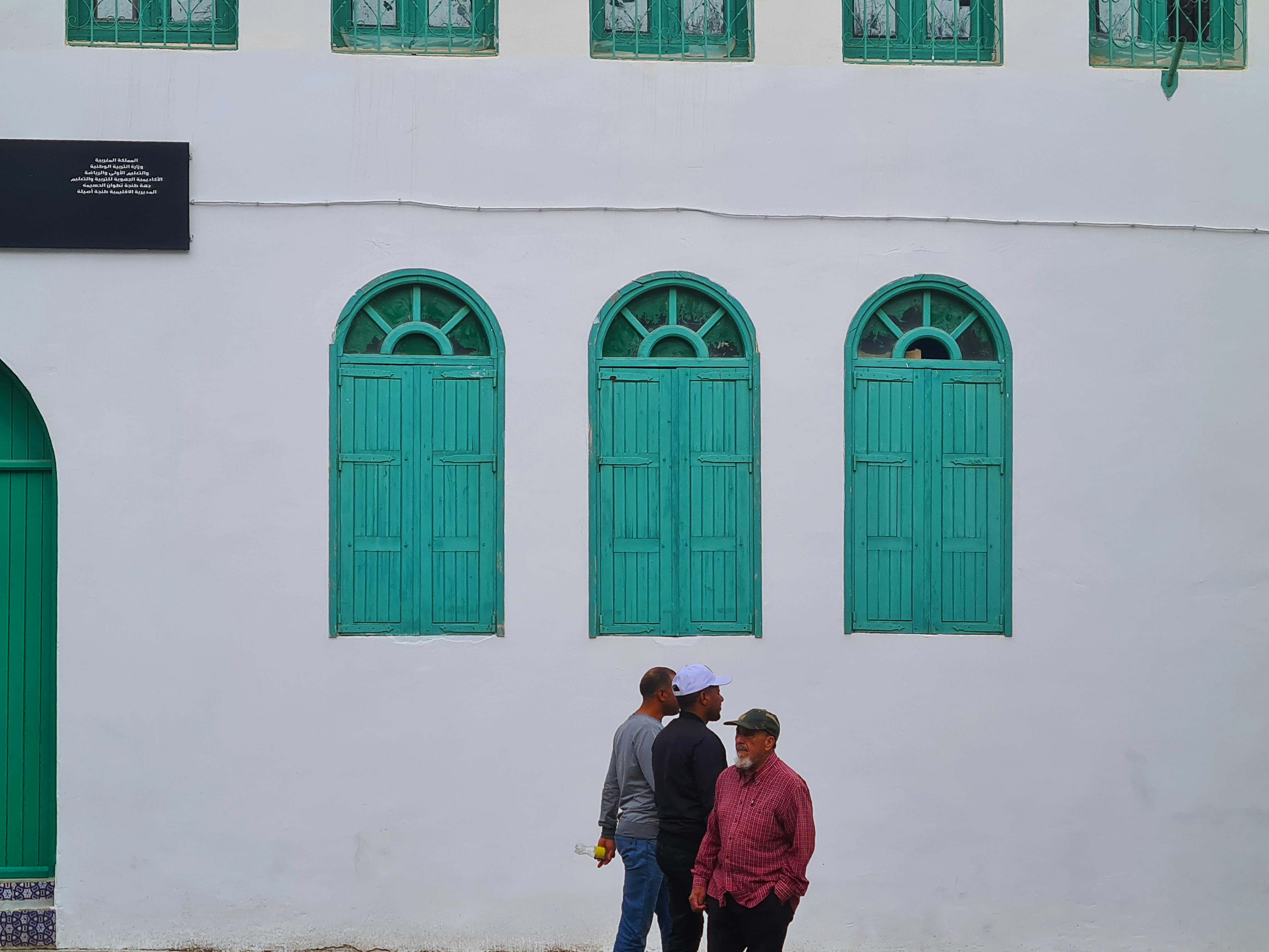 Three men stand in front of a white building.