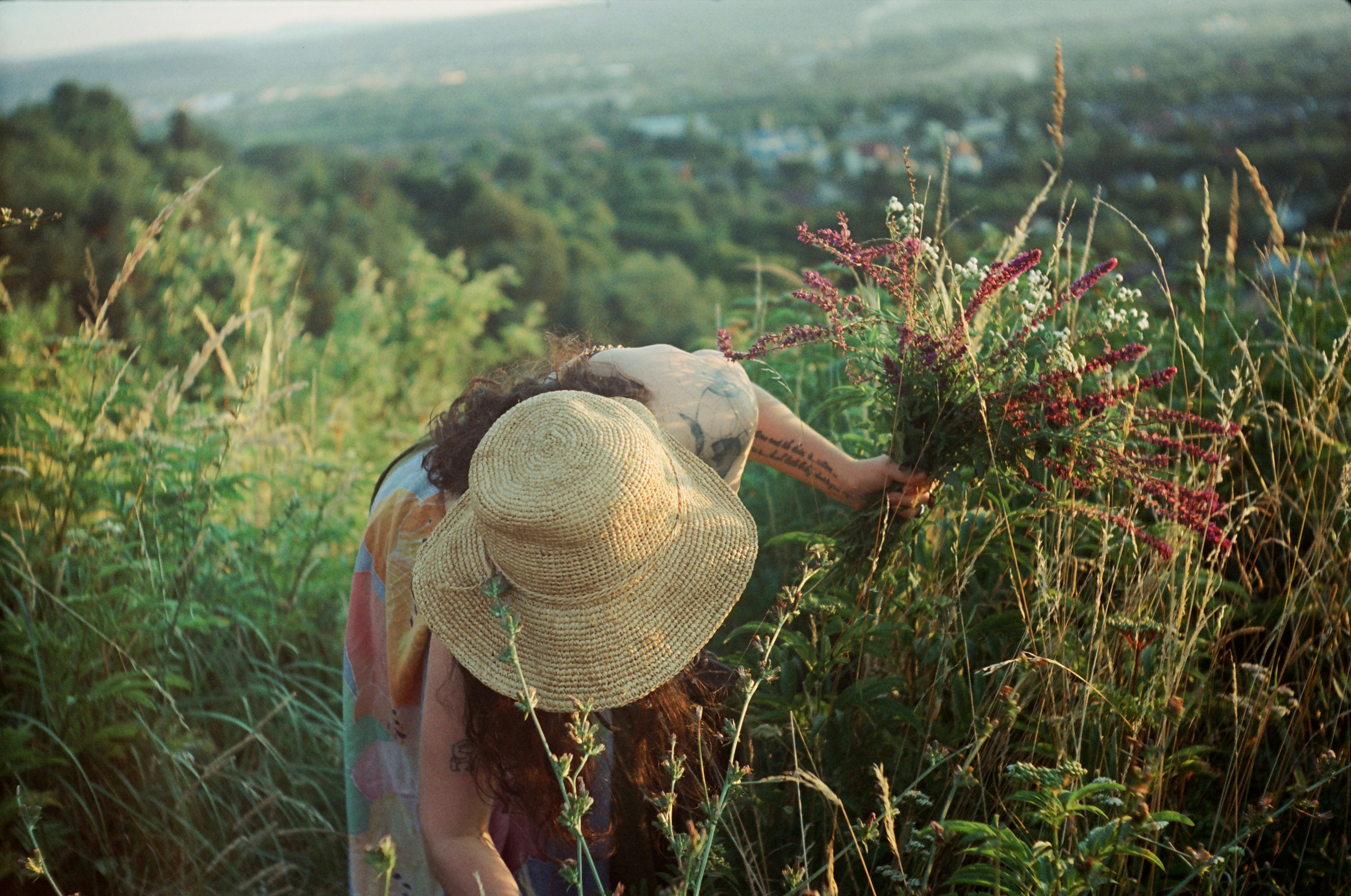 Woman in straw hat picking wildflowers in grassy field