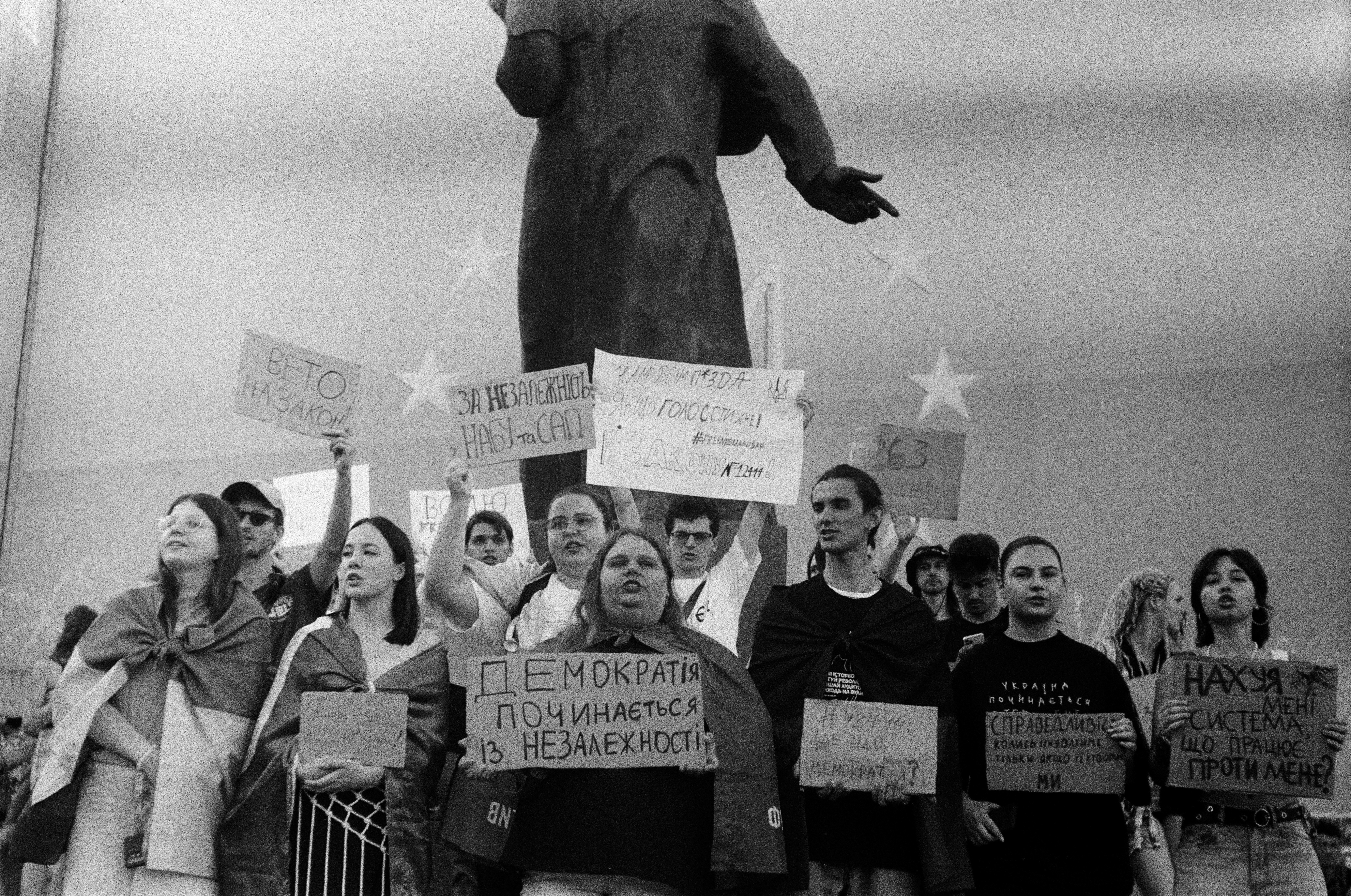 Protesters hold signs near a statue under stars.