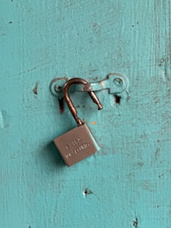 An unlocked padlock on a teal wooden surface.
