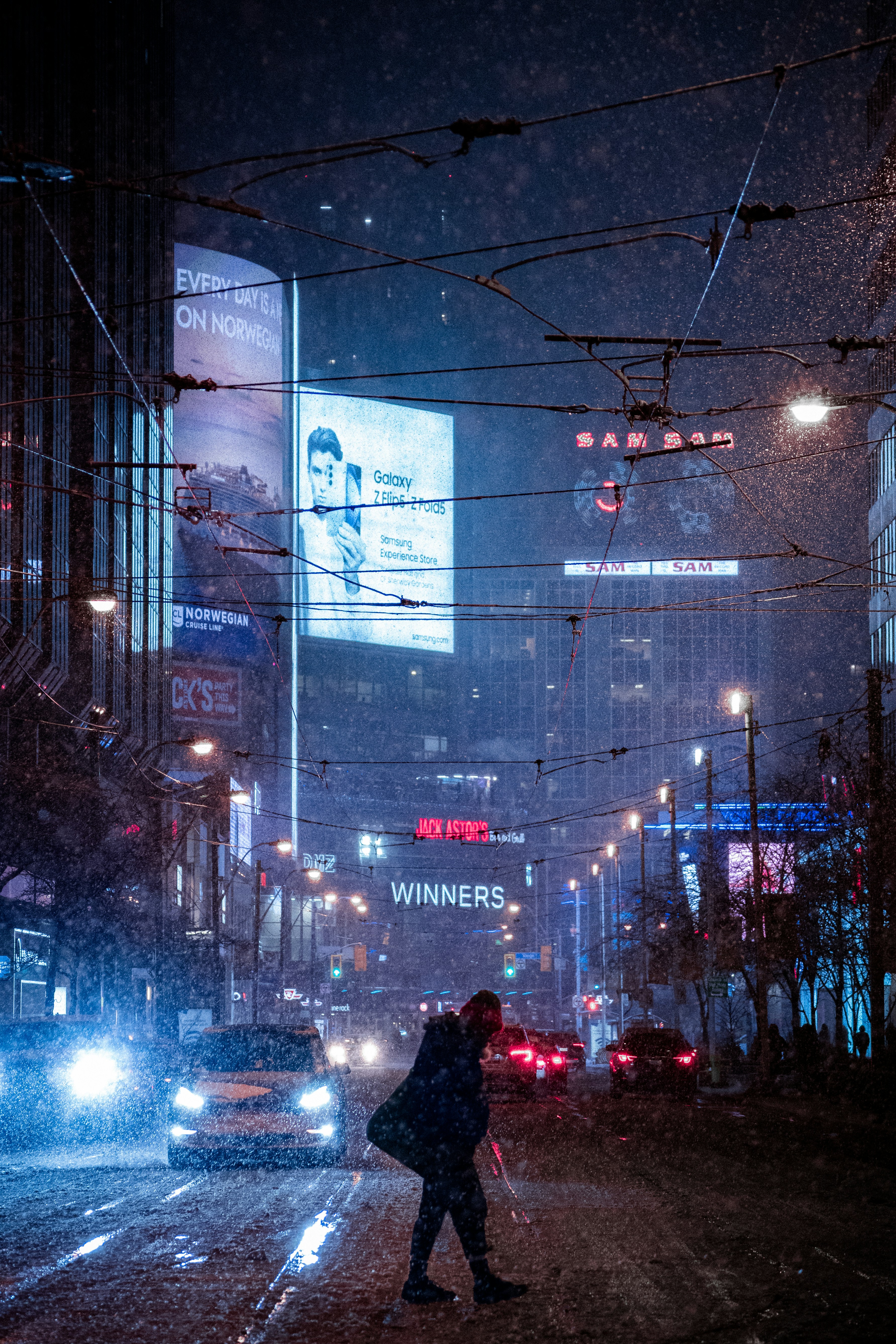 Person crosses street in rainy city at night