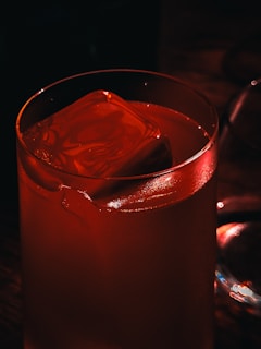 A red cocktail with a large ice cube.