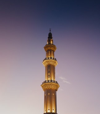 Tall mosque minaret illuminated against twilight sky