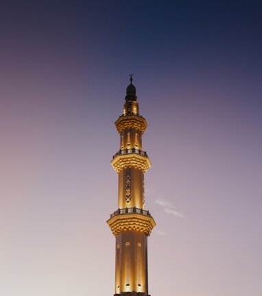 Tall mosque minaret illuminated against twilight sky