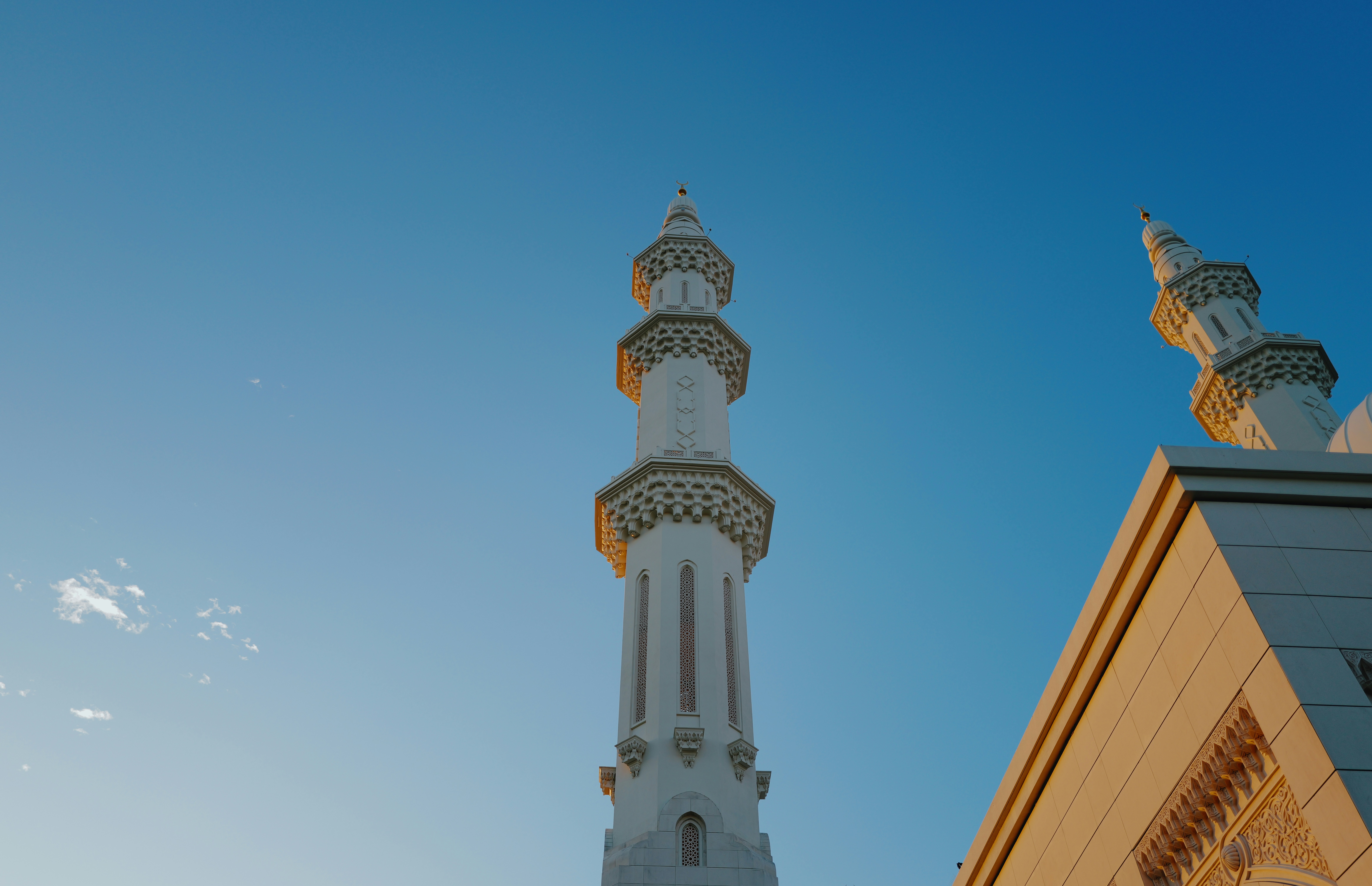 Two white mosque minarets against a clear blue sky
