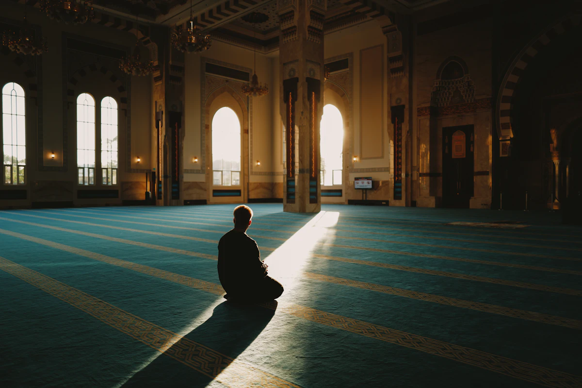 A person sitting quietly in a sunlit mosque prayer hall