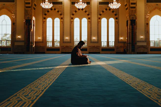 Man praying alone in a grand mosque with sunbeams
