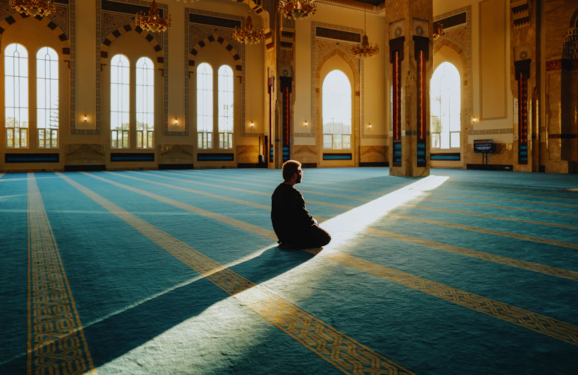 Man praying in a large, sunlit mosque