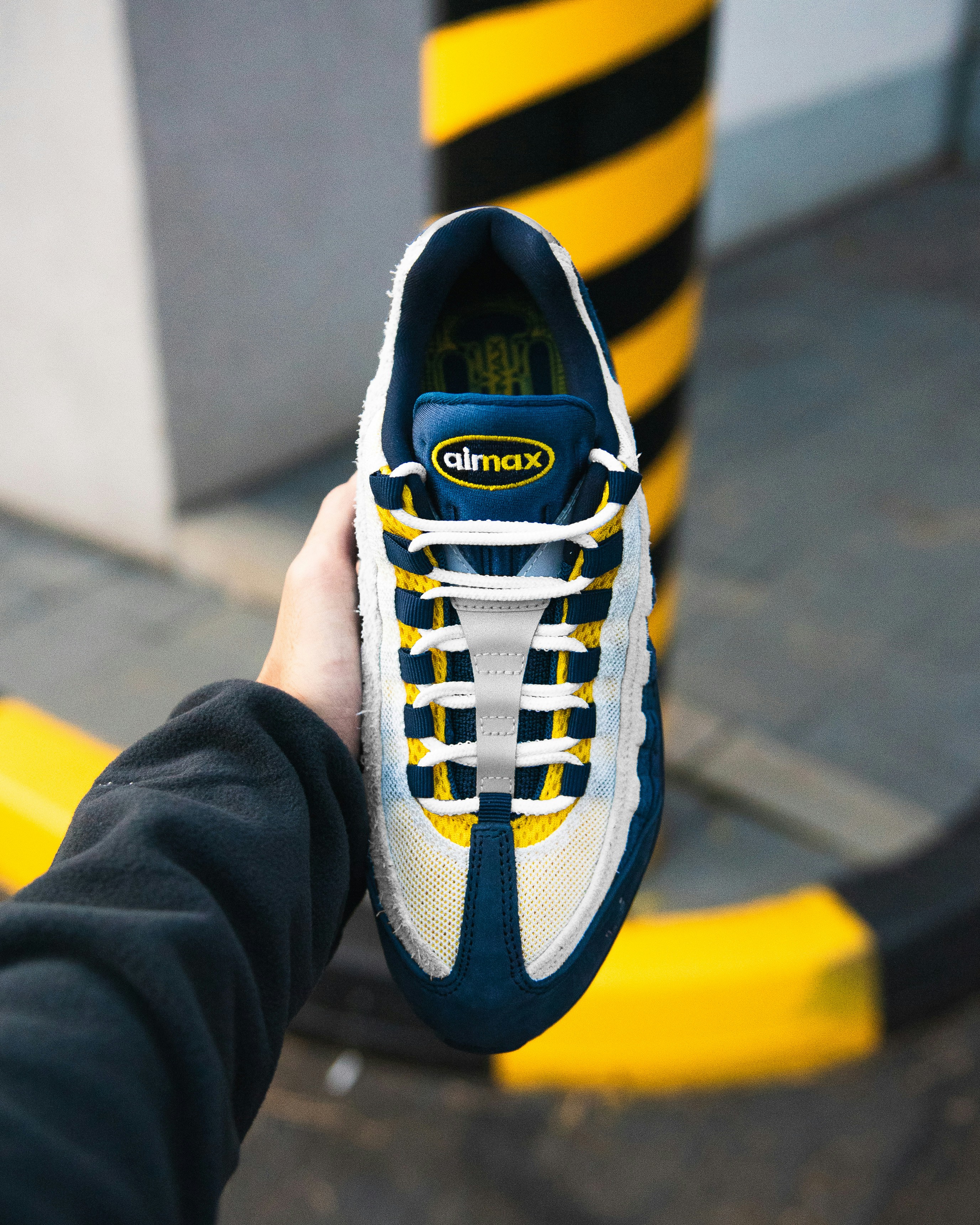 Hand holding a blue and yellow nike air max sneaker.