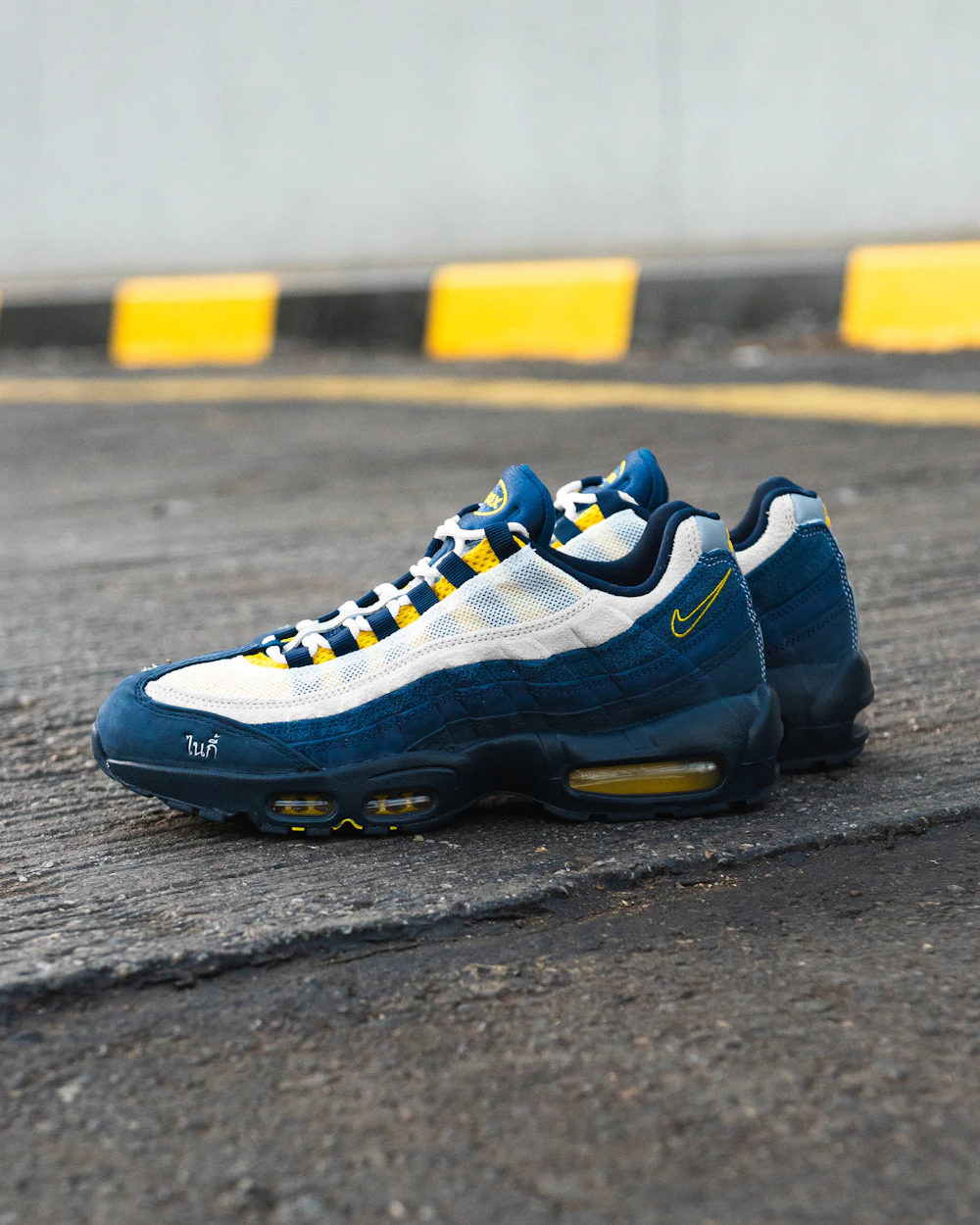 Пара кроссовок Nike Air Max 95 в тёмно-синем, белом и жёлтом цветах на потрескавшемся асфальте