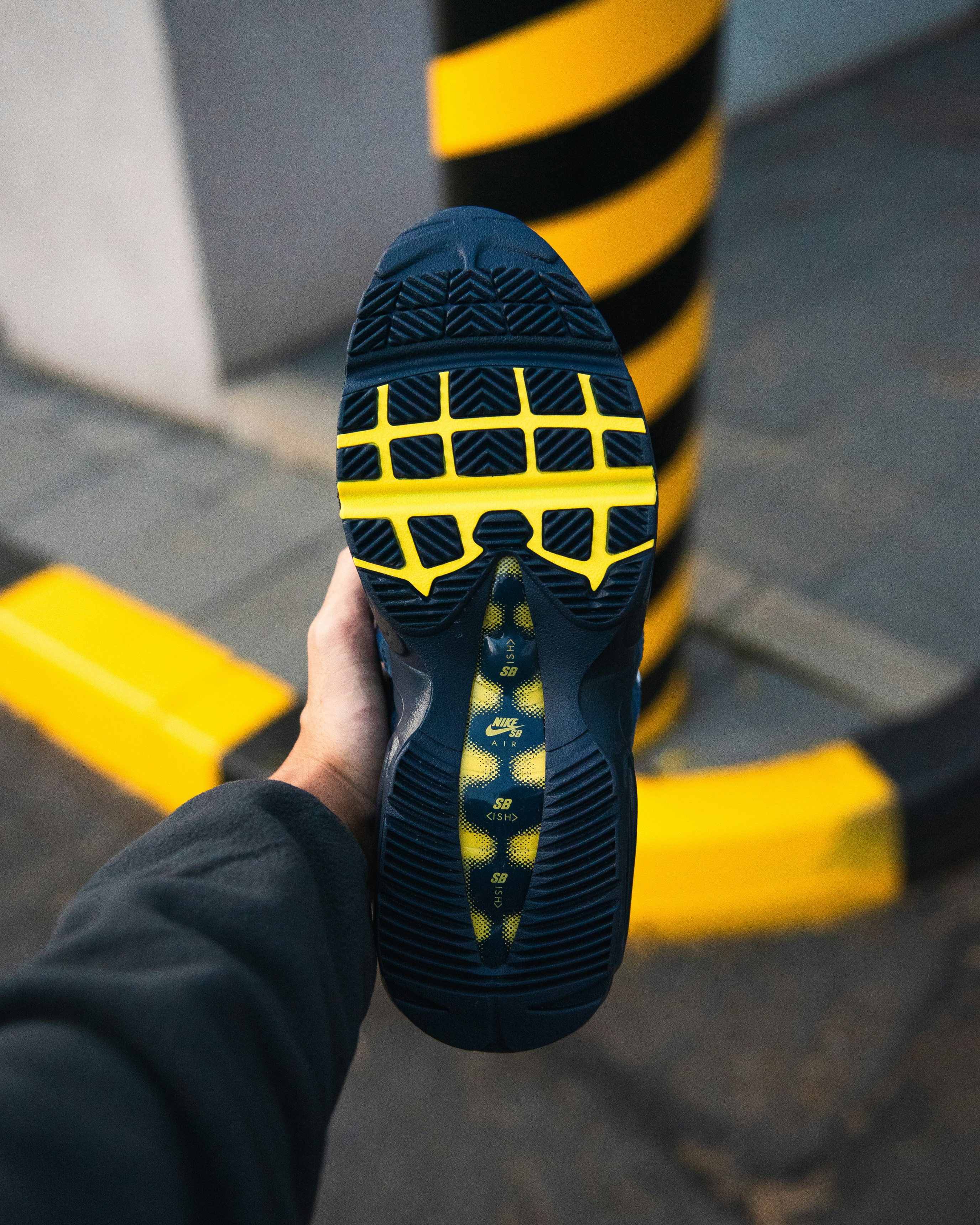 Hand holding a dark blue sneaker with yellow accents.