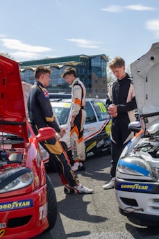 Three young men in racing suits by cars