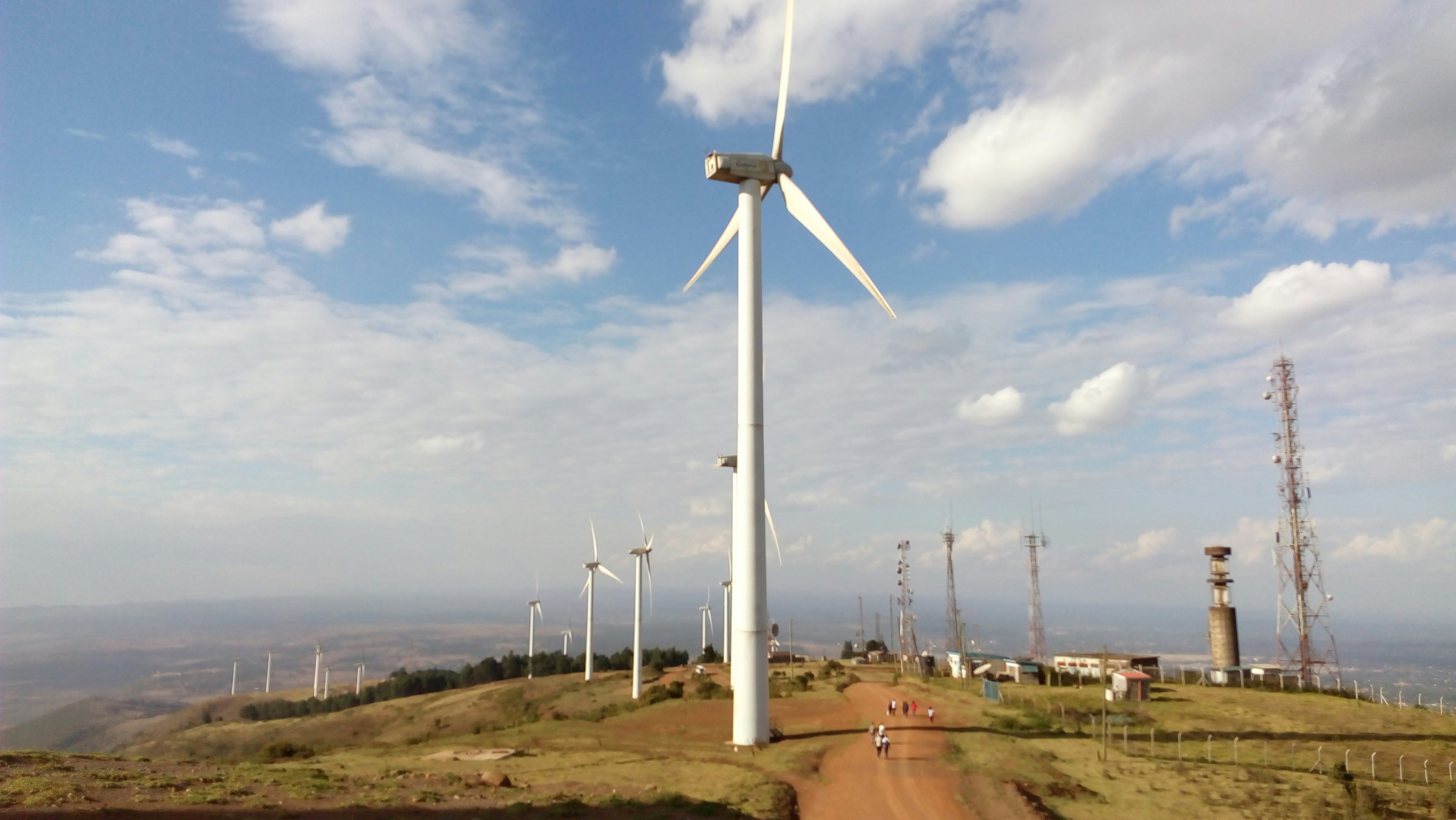 renewable energy wind farm infrastructure - Wind turbines stand on a grassy hill under clouds