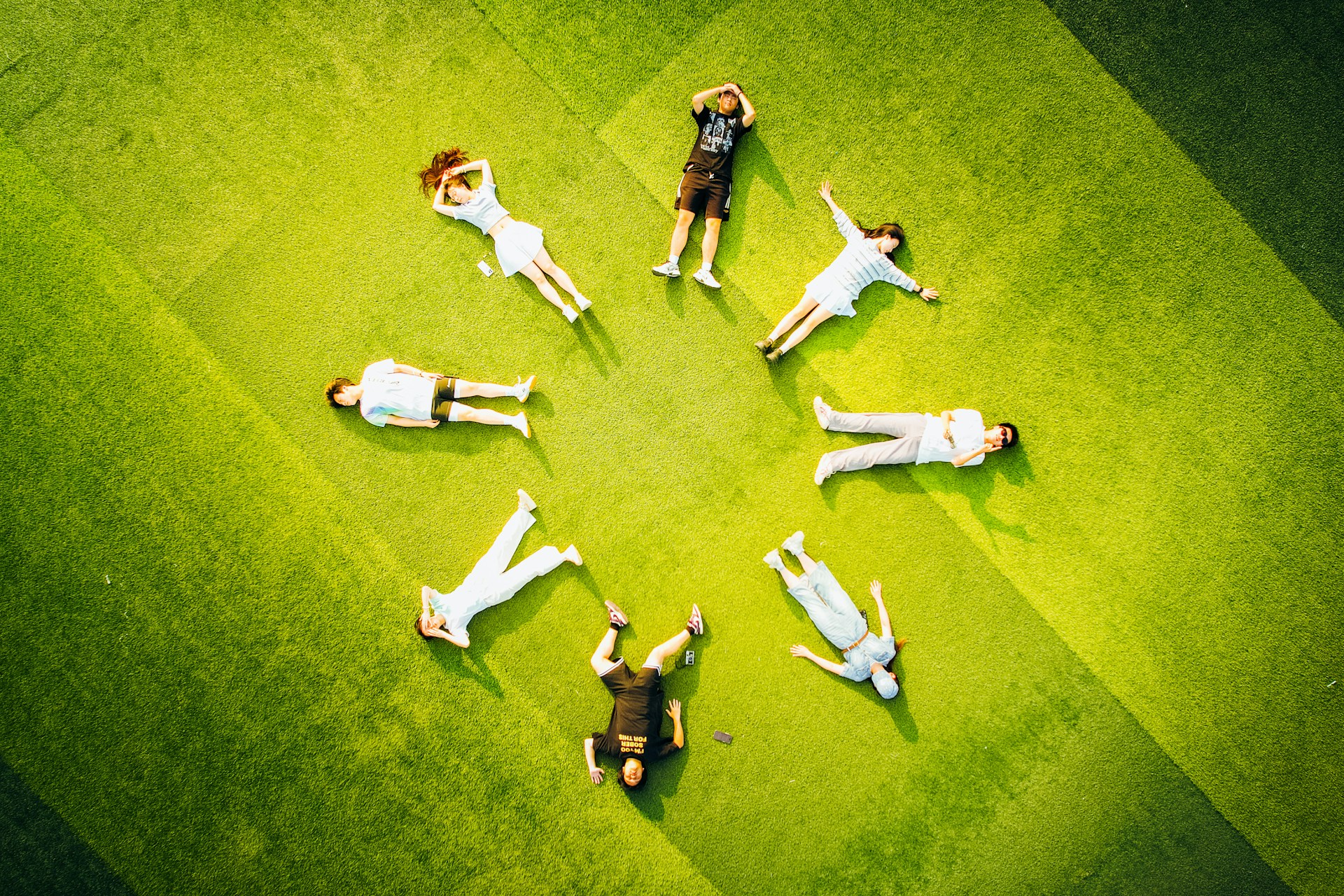People lying in a circle on green grass.
