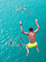 Boy jumps into bright blue ocean with swimmers
