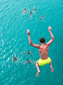 Boy jumps into bright blue ocean with swimmers