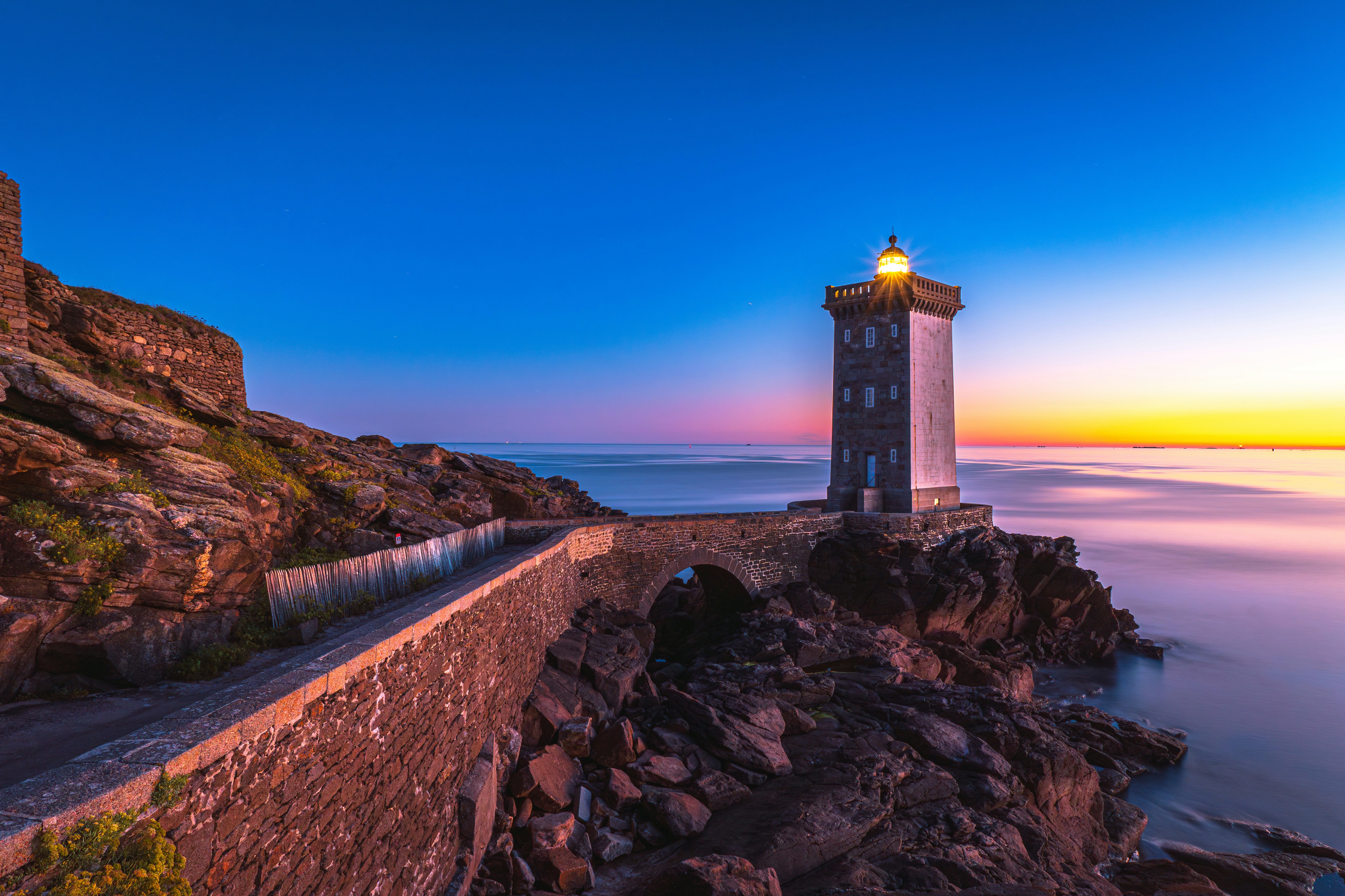 Lighthouse on rocky coast at sunset with calm ocean