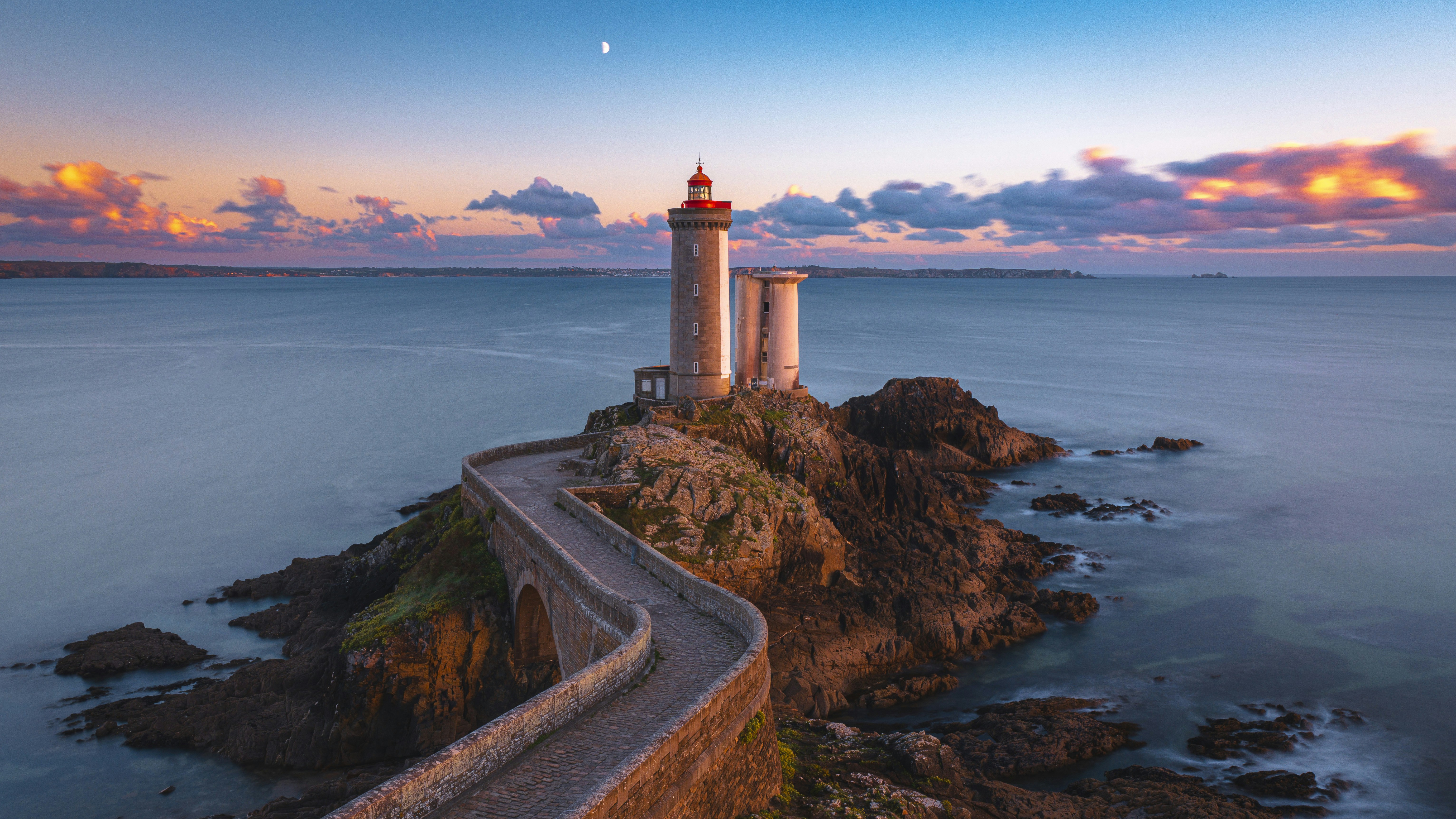 Lighthouse on rocky island with causeway at sunset