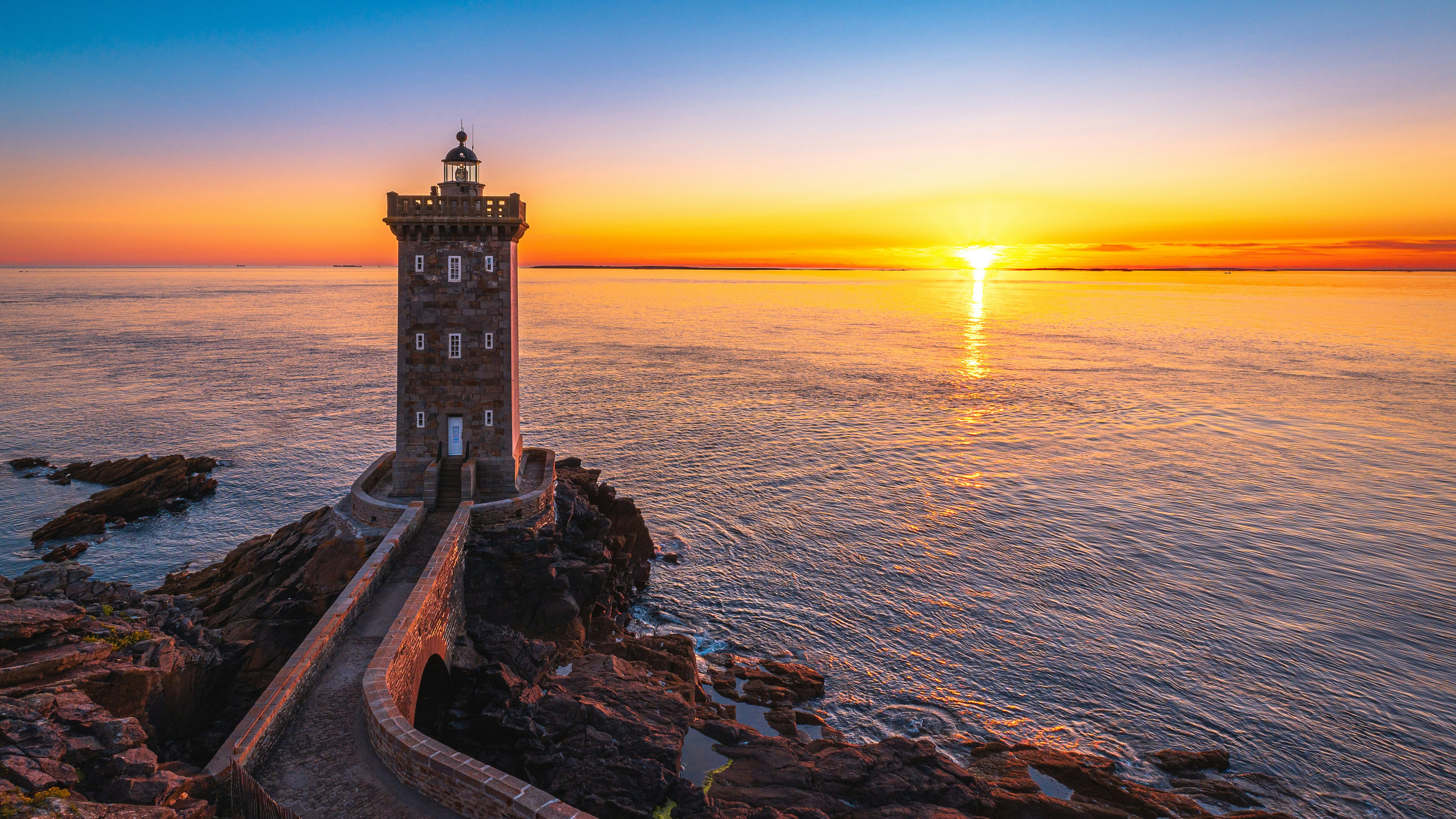 Lighthouse on rocky coast at sunrise with ocean reflection