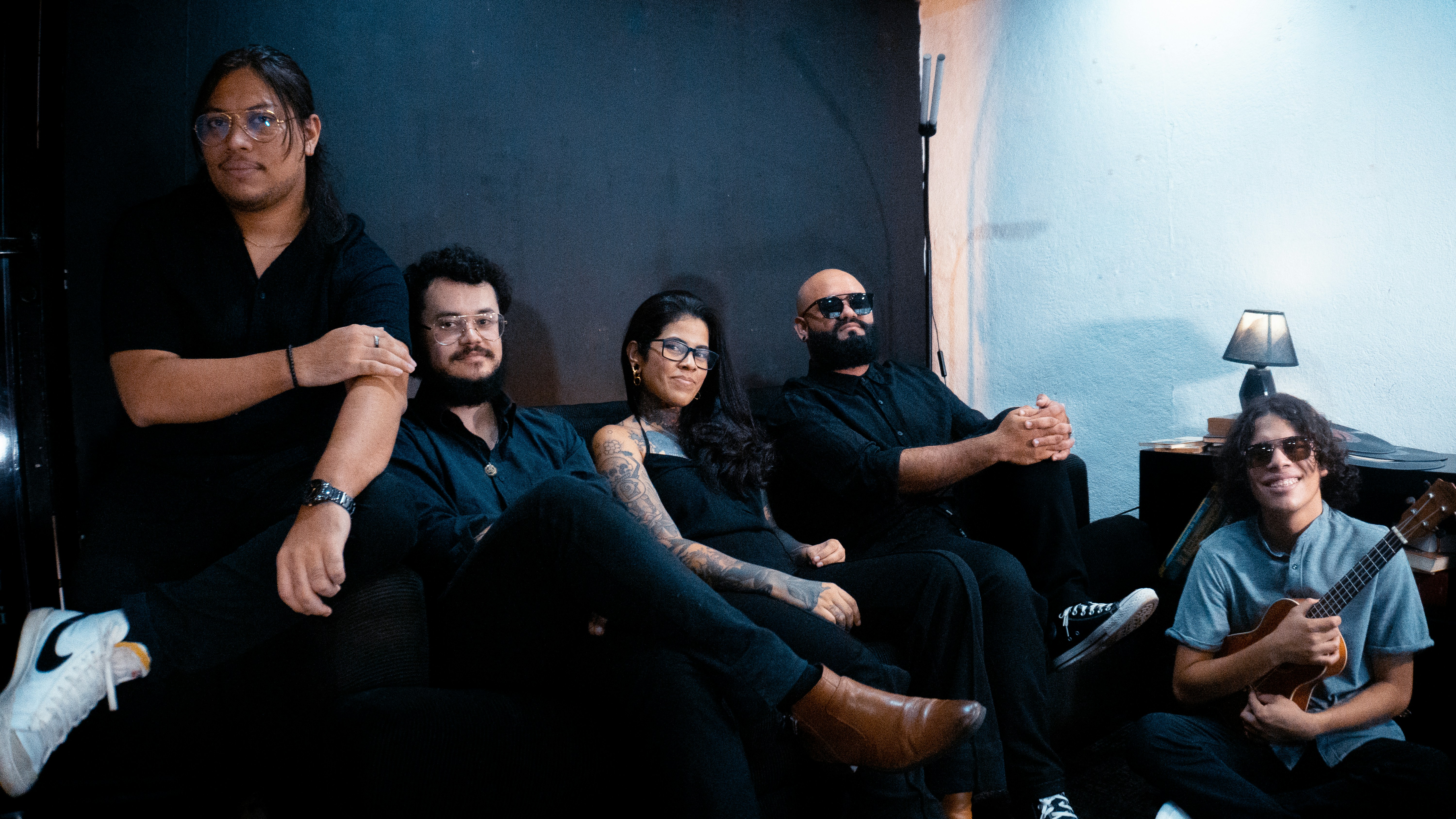 Five people sitting on a couch wearing dark clothing