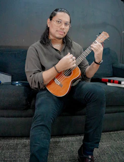 Man playing a ukulele while sitting on a couch.