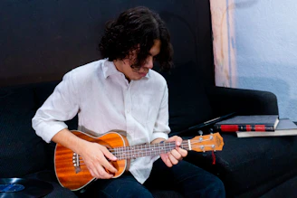 Young man playing ukulele on a couch.