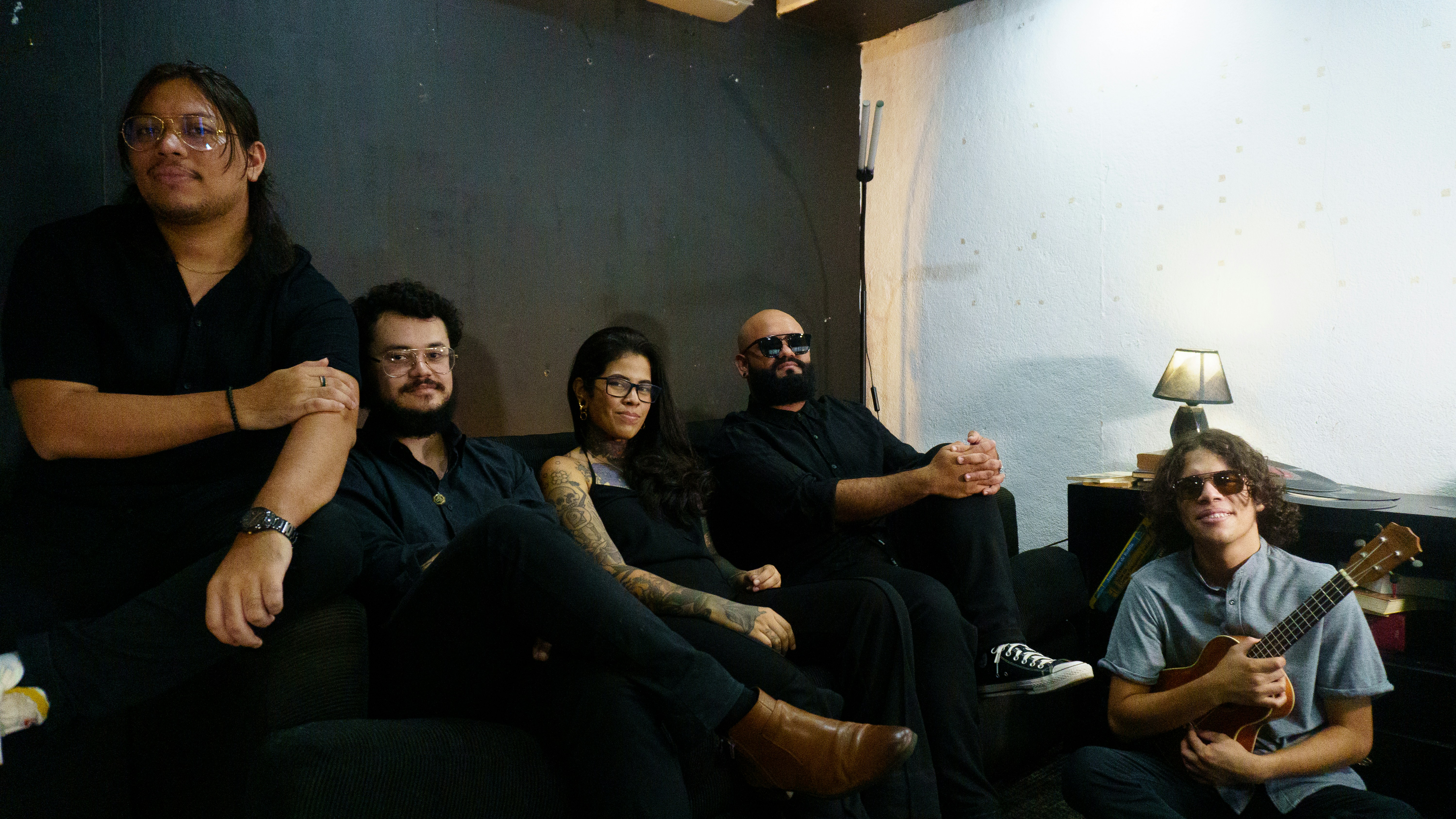 Five people sitting on a couch, one holding a guitar.